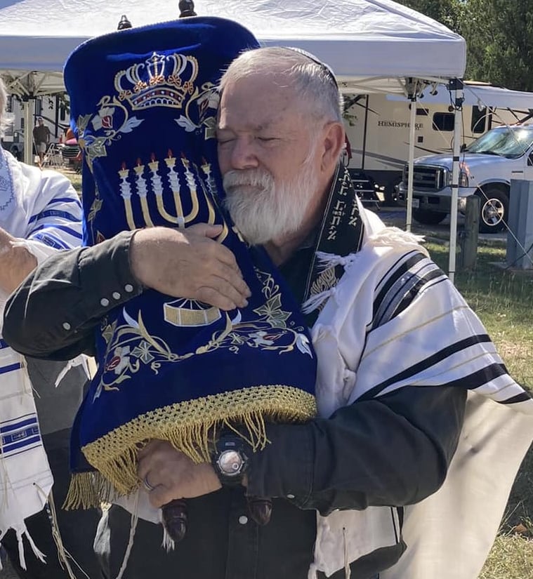 Rabbi Jay Ledbetter, eyes closed, holding the scroll close in its blue covering embroidered with a crown and a menorah, a prayer shawl over his shoulders