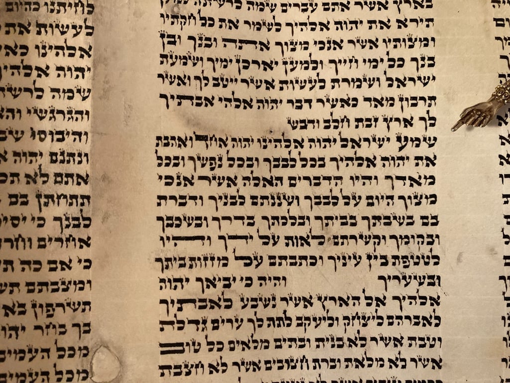 Columns of hand-lettered text in our scroll, crowns on many of the letters, with a silver pointer shaped like a hand beside the Shema